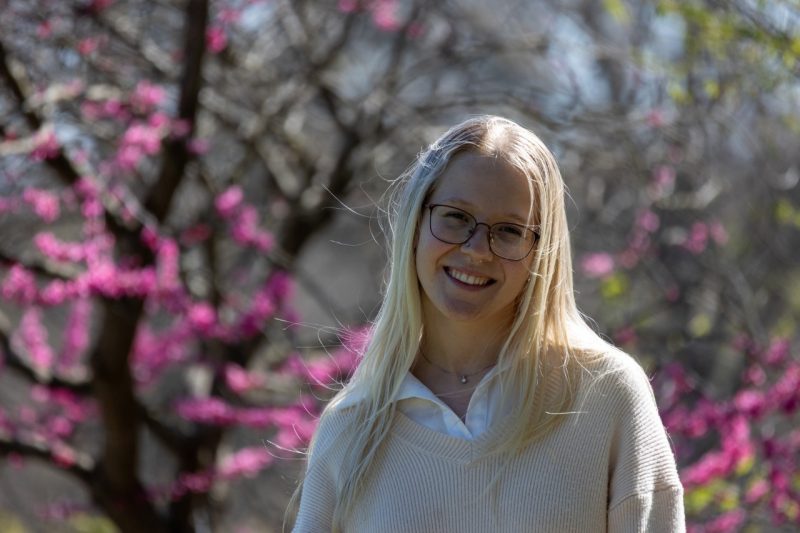 young blonde woman in a light tan sweater in front of a blooming tree
