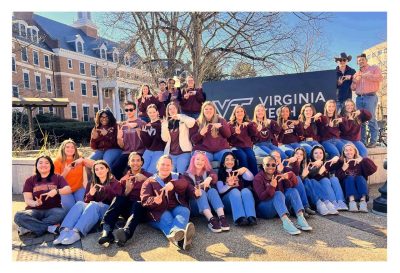 The 2024-2024tudent Ambassador Team as a group doing "VT" with their hands around a Virginia Tech sign on campus.