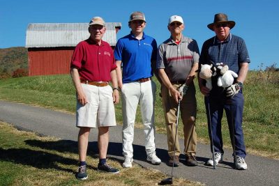 Team Virginia Tech maroon standing together with the red  barn in the backgound on the golf course.