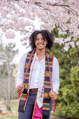 Brandon Duncan wearing his graduation stoles and standing under a cherry tree.