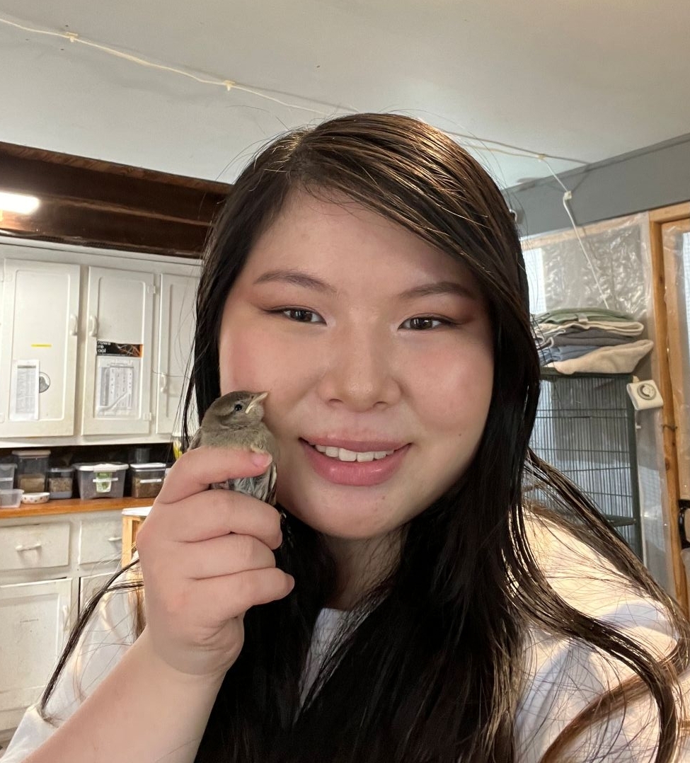 Young woman holding a bird up to her face.