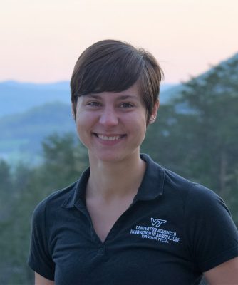 White woman with short hair wearing a black polo shirt with mountains in the background.
