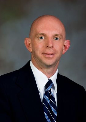 Professional photo of Dave Winston wearing a suit against a blue-gray background.