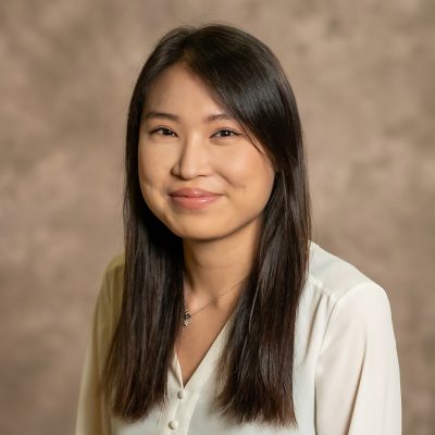 Professional photo of Yeeun Bae. Mottled, burred, greige backgound. Young woman with long dark hair smiling toward camera.