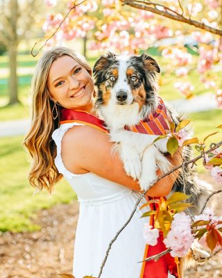 Lexie Butler wearing graduation sash and her dog wearing a striped Hokie bandana. Spring blooms.