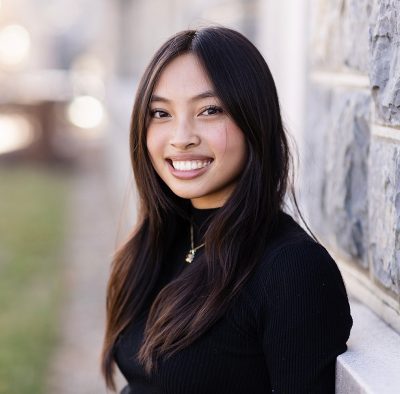 Young woman with long dark hair smiling in front of a HokieStone wall on campus at Virginia Tech. Blacksburg.