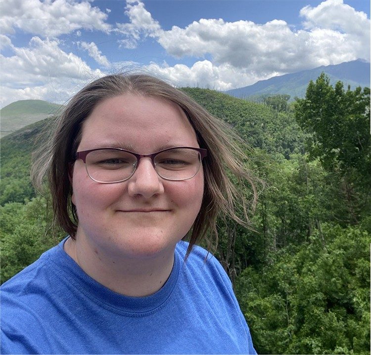 Photo of Shannon Chick with green trees on the next ridge in the background. Blue sky with white clouds.