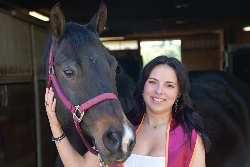 Abbey Collier wearing her academic stole with a horse wearing a matching halter.