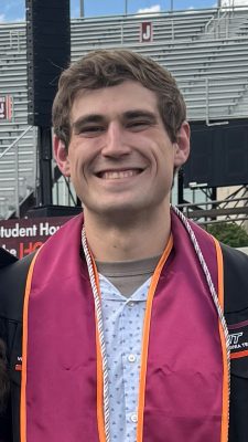 Smiling young man wearing graduation robe, stole, and cord at Lane Stadium. Bleacher section J in the background.