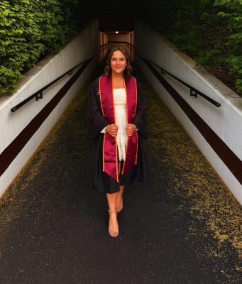 Smiling young woman in her graduation gown and sole exiting tunnel on Virginia Tech campus.
