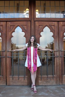 Young woman wearing her graduation sash and cords at Burrus Hall enrance.