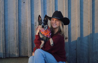 Young blond woman wearing a black cowboy hat with a cattle dog wearing a VT bandana.
