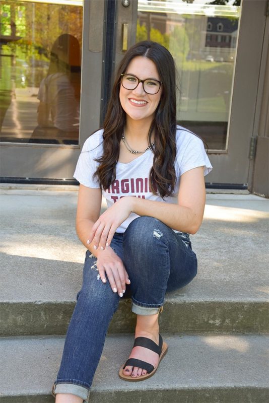 Graduate student, Abigayle Pollock sitting on steps, smiling.