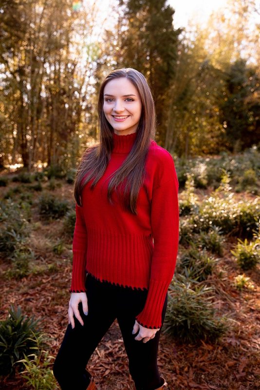 Young woman in a red sweater smiling. Fall or winter blurred background trees..