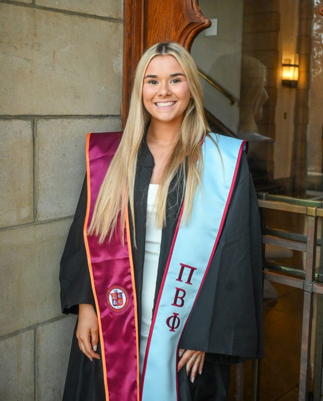 Smiling young woman with long blond hair in her graduation regalia.