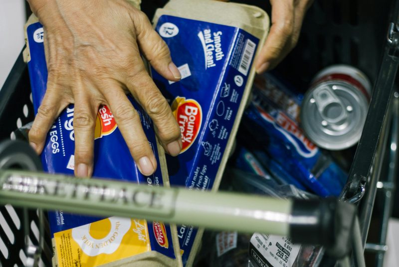 Egg cartons being placed in a shopping basket among other groceries. 