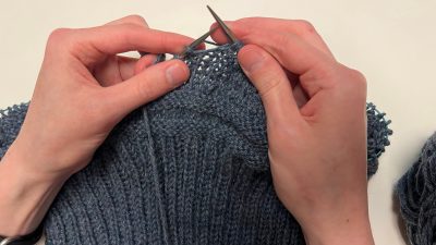 A close-up of two hands knitting with dark gray yarn.