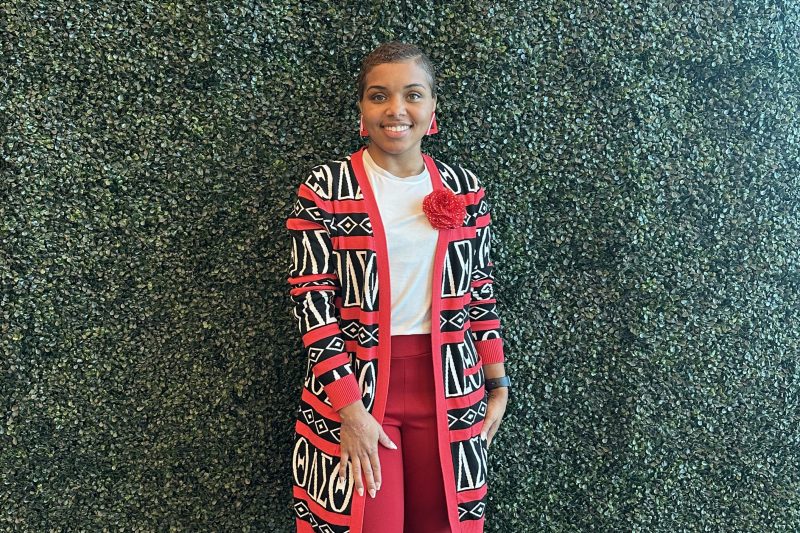 A woman, smiling, stands in front of a green wall.