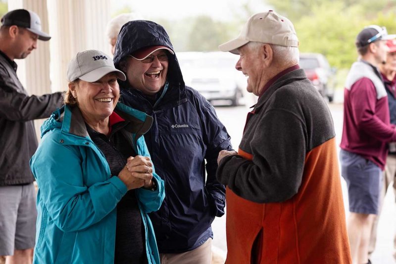 Golfers laughing together under the portico out of the rain. 2023.