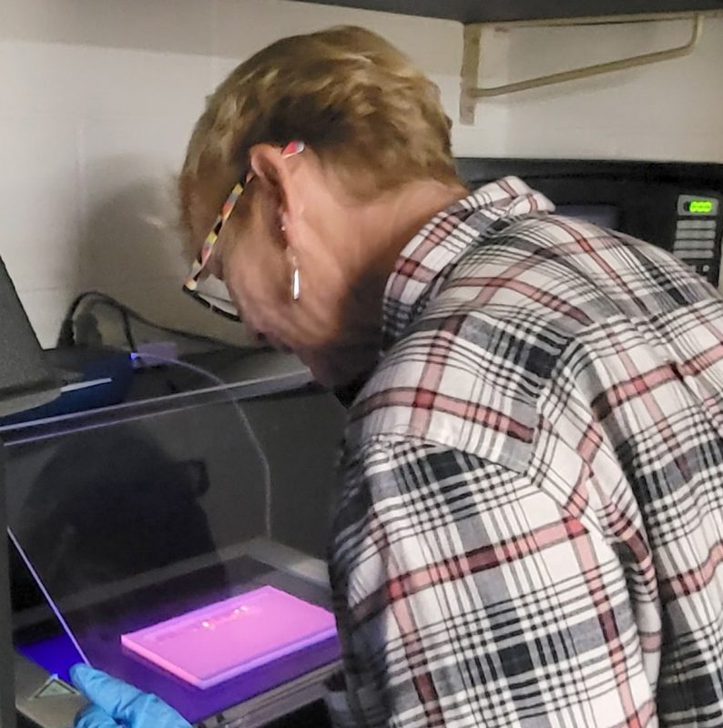 Graduate student wearing a lab coat and gloves pipetting into sensor structure.