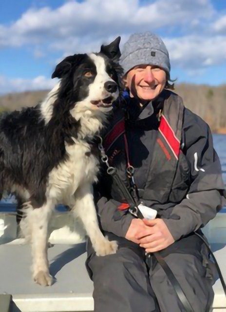 Photo of Sally Dickinson wearing a toboggan with her Border Collie dog on a cold day.