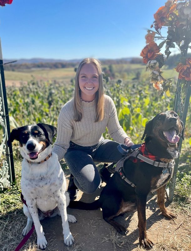 Photo of Briana Kincaid  with two dogs with fields in the background.