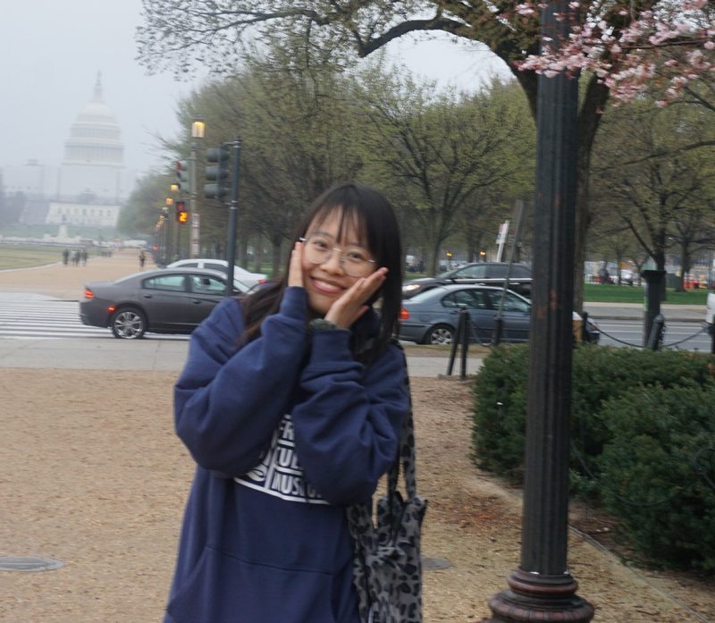 Photo of graduate student, Shihong Yang, under a cherry tree beginning to bloom in Washington, D.C.