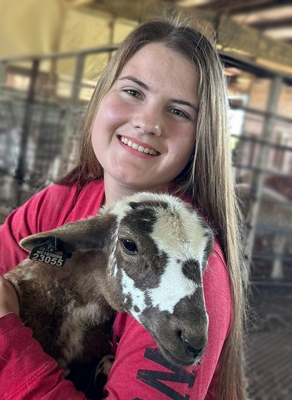 Erin Poteat in the barn, holding a brown and white faced sheep.